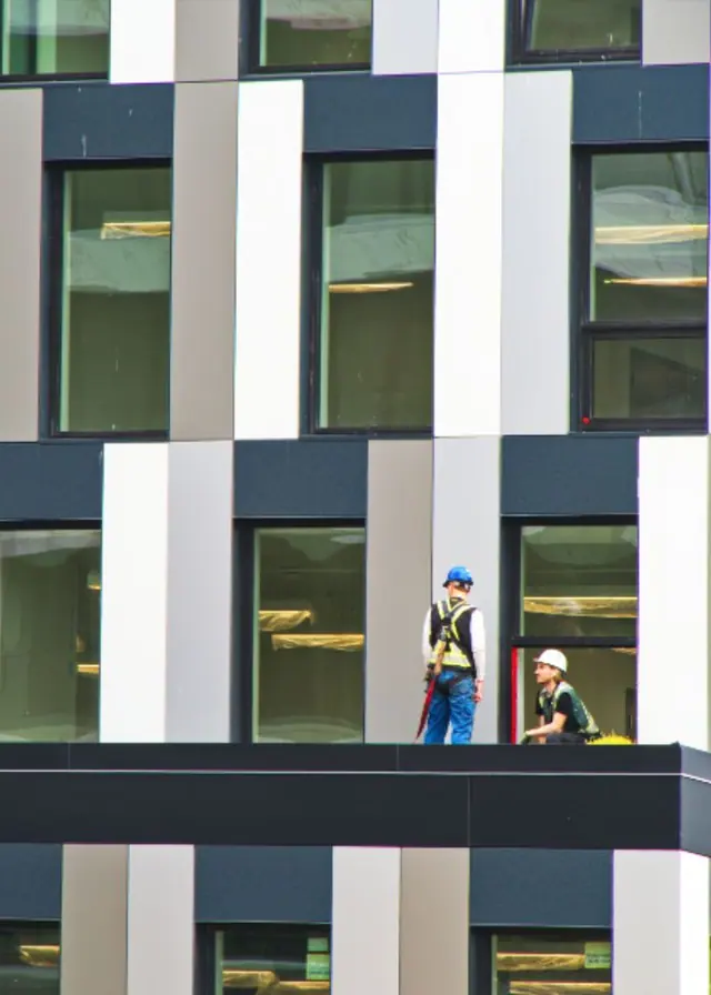 Deux ouvriers en gilet sur le balcon d'un immeuble neuf